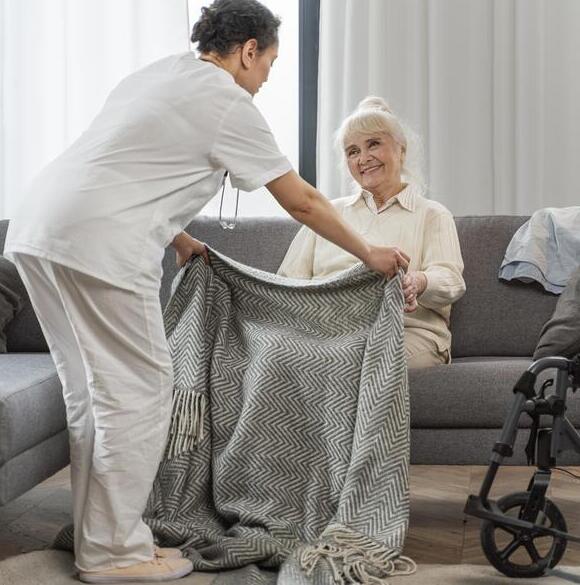 Infirmière à domicile de Central Infi installant confortablement une patiente âgée souriante sur son canapé avec une couverture.