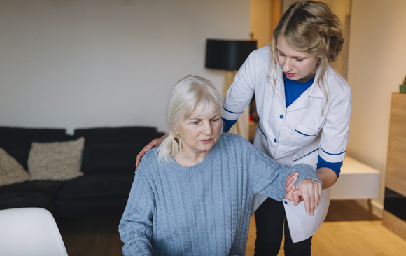 Infirmière à domicile guidant et soutenant le bras d'une patiente senior en convalescence lors d'une hospitalisation à domicile.