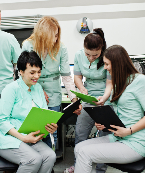 Équipe d'infirmières et infirmiers souriants, en uniforme médical, collaborant autour de dossiers de soins à domicile.