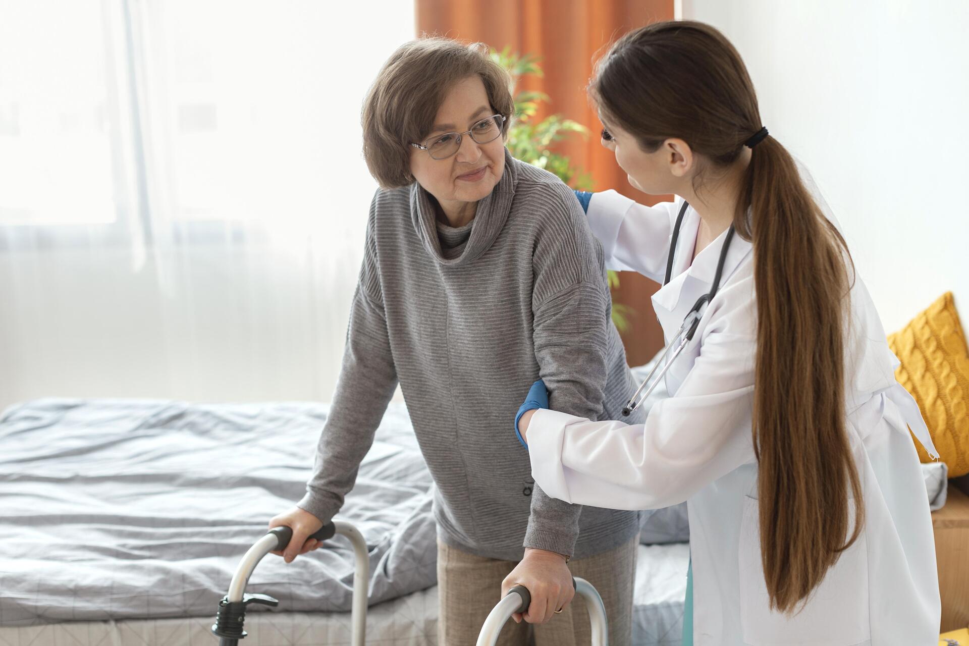 Infirmière à domicile de Central Infi aidant une patiente âgée à se déplacer avec un déambulateur dans sa chambre.