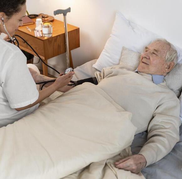 Infirmière à domicile de Central Infi prenant la tension d'un patient âgé alité dans le cadre de soins palliatifs et de suivi médical.